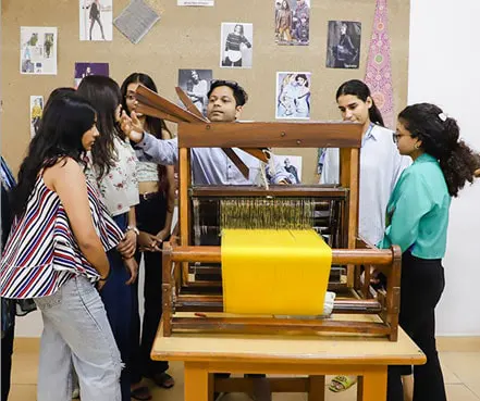Students learning handloom textile weaving with faculty guidance at a fashion designing institute in India