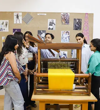Students at a fashion designing institute in India learning textile weaving on a handloom with a faculty mentor